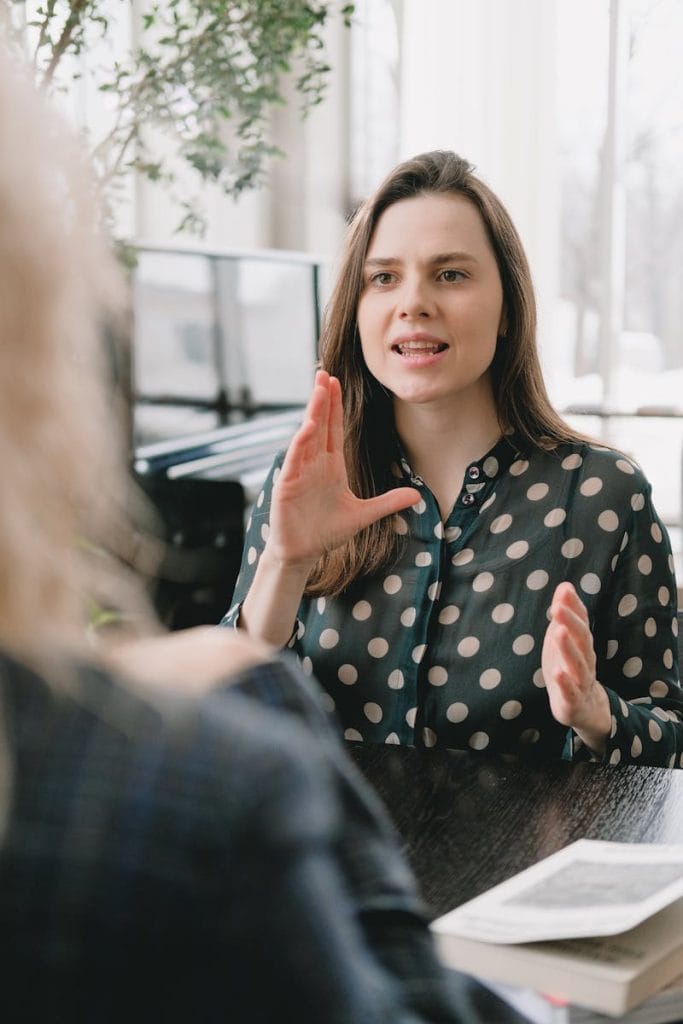 Focused woman in a polka dot blouse engages in a conversation indoors.